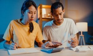 A young couple sits at a desk using a calculator while budgeting